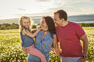 Wall Mural - family outdoors spending time together Father, mother and daughter are having fun during the sunset.