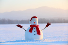 Snowman In Red Hat And Scarf. Christmas Scenery. High Mountains At The Background. Ground Covered By Snow. Nice Cold Winter Day.