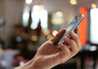© meepoohyaphoto - Hand of man holds a smartphone on blur restaurant background and have copy space.