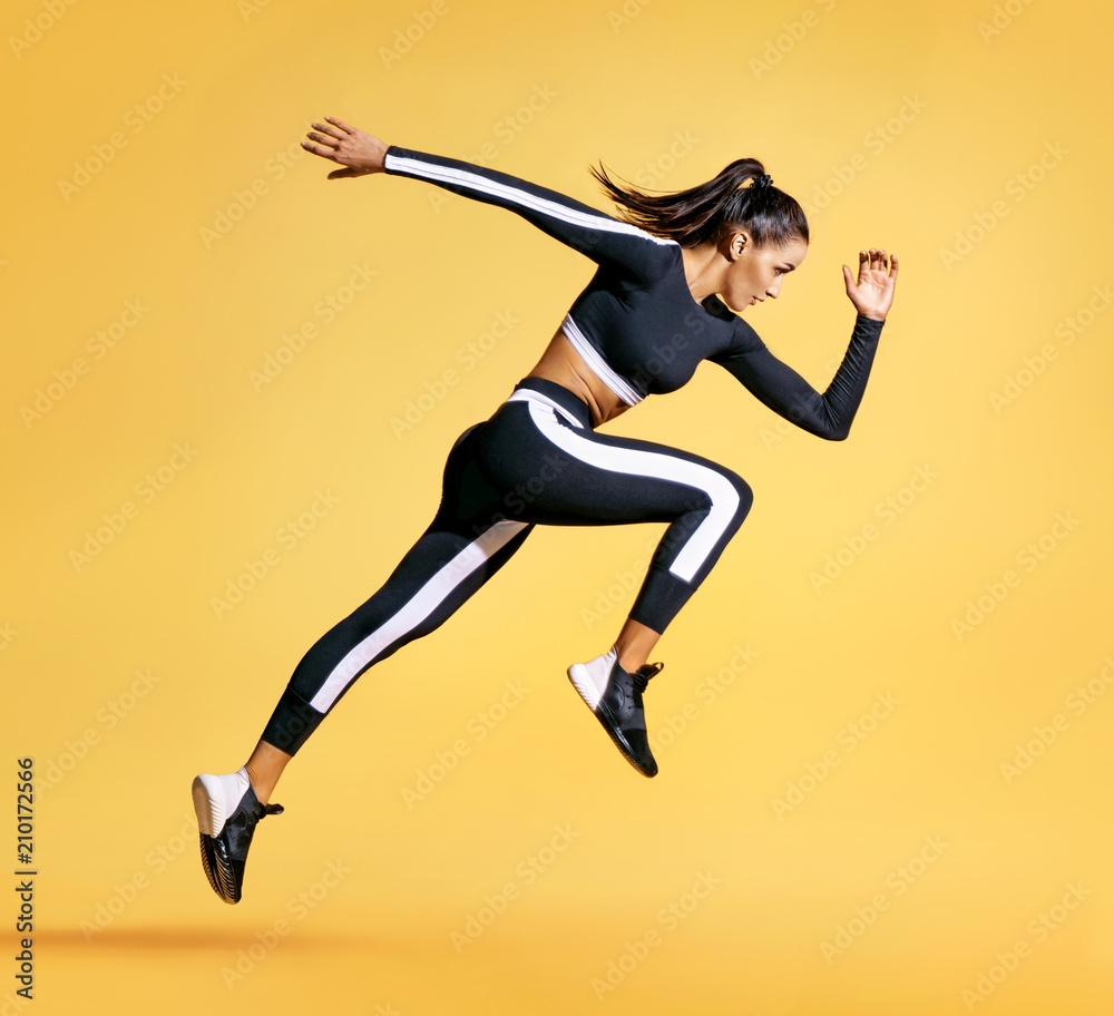 Sporty woman runner in silhouette on yellow background. Photo of attractive woman in fashionable sportswear. Dynamic movement. Side view. Sport and healthy lifestyle - obrazy, fototapety, plakaty 