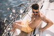 © LIGHTFIELD STUDIOS - shirtless muscular man in swim trunks and sunglasses having sunbath on yacht