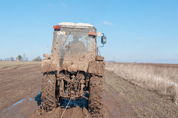 Wall Mural - Wheeled tractor tows in mud on dirt road in fallow field