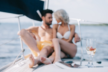 Sticker - selective focus of champagne glasses and couple sitting behind on yacht