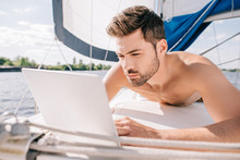 Young Shirtless Man Having Sunbath And Using Laptop On Yacht