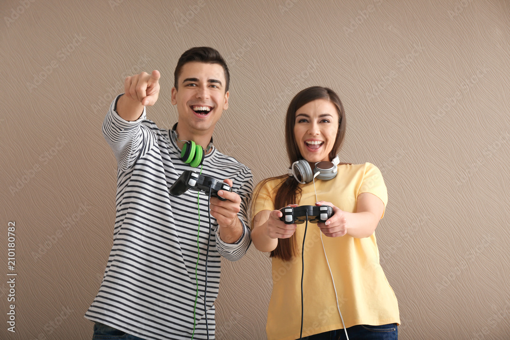 Young people with gamepads on color background