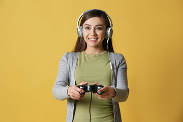 Young woman with gamepad on color background