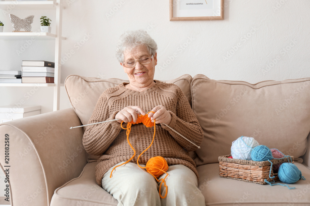 Senior woman sitting on sofa while knitting sweater at home Stock Photo ...