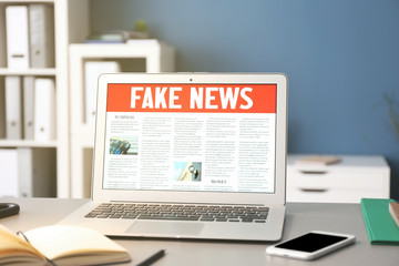 workplace with laptop and fake news on screen