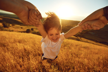 Father turns a child in the field in nature at sunset.