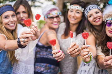 Wall Mural - group of mixed ages women from young to old stay together in friendship taking and offering a candy hearth lollypop to you. peaceful and lifestyle inspired to peace and love like hippy style