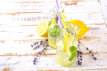 Ice cold lavander lemonade, lemon, straw. Two classic virgin mojito drinks, non alcoholic cocktail with ice in two vintage hipster bottles, on grunged wood background. Copy space, top view close up.