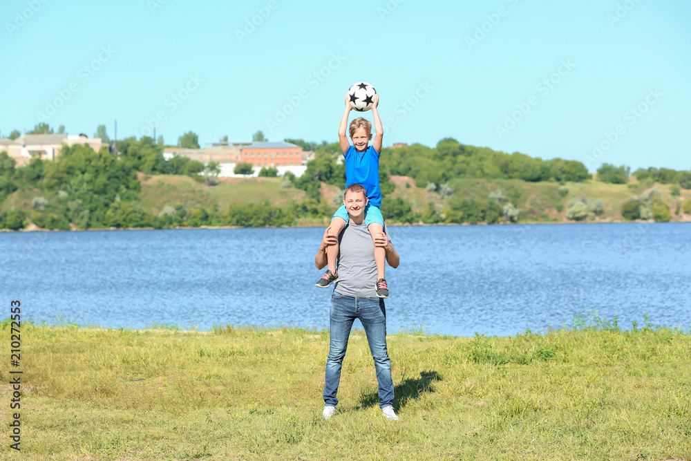 Happy father and son with soccer ball near river