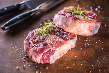 Two raw pieces beef shank on wooden butcher board with fork and knife.