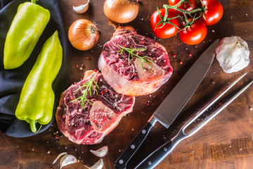 Two pieces raw beef shank and basic ingredients on goulash - onion pepper tomatoes garlic salt spices and rosemary