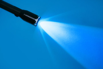 flashlight and a ray of light in the dark on a blue background. A modern LED lamp with a bright projection. Surface with a copy.