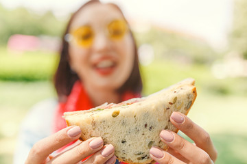 Young woman eating sandwich and having lunch break outdoors in park