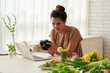 © DragonImages - Portrait shot of pretty Asian food blogger looking through photos on modern camera while working on her vlog at home