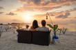 Romantisches Paar sitzt in einem Sofa am tropischen Strand bei Sonnenuntergang und genießt den Urlaub