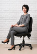 © soleg - the business woman sitting on a chair, dressed in a gray suit poses in front of a white wall