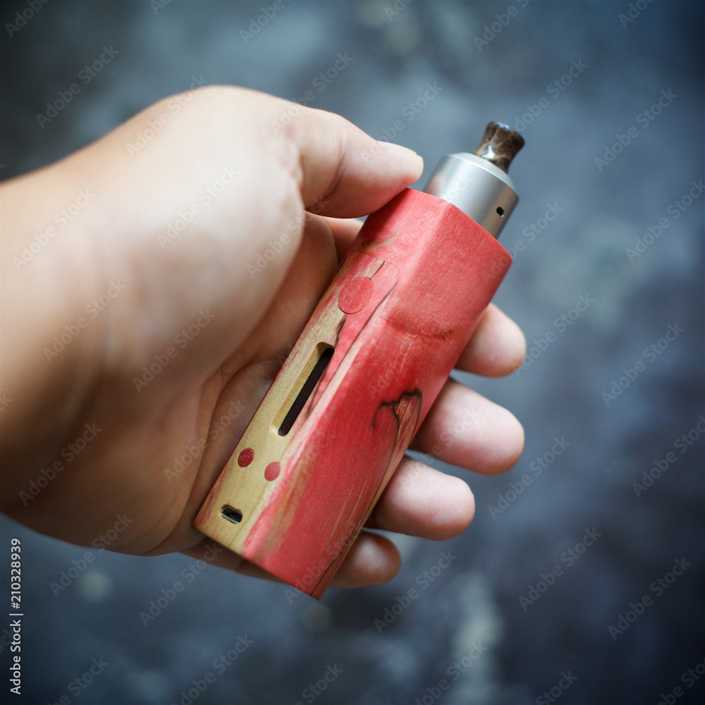 wood vape mod high end red natural stabilized box mods with rebuildable dripping atomizer gear in hand on dark grey texture background, vaporizer equipment, selective focus with shallow depth of field Stock Photo Yocan UNI Pro-Digital Box 30ML SALTNIC DUBAI Flavour:Wild Berry Ice