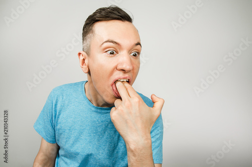 Valokuva Young guy inserts two fingers in the mouth to induce vomiting, on a light background