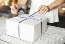 Young Cook Ties Violet Ribbon On White Cake Packaging