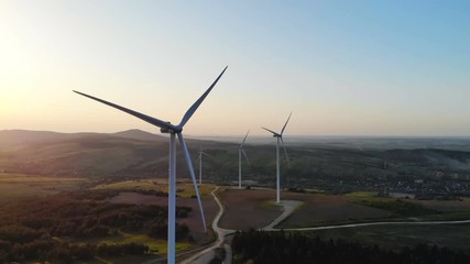 Wall Mural - huge white wind turbines in motion from aerial shooting with beautiful summer sunset with mountains on background village area windmill farm of electricity new technology generation healthy eco life