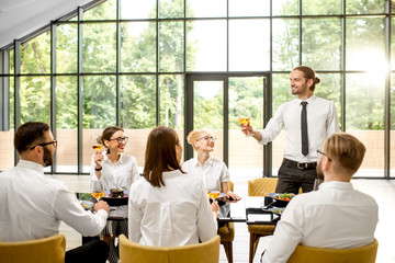 Business people dressed in white shirts sitting together during a business lunch with man speaking toast at the modern restaurant