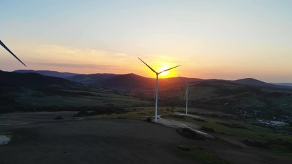 Wall Mural - fiery sunset over mountains with the silhouettes of wind turbines blades rotating converting kinetic energy into electricity aerial shooting bright sunlight rising ecology life idyll peaceful horizon