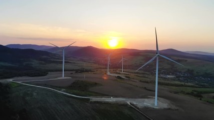 Wall Mural - scenic fiery sunset over mountains with the silhouettes of wind turbines blades rotating converting kinetic energy into electricity aerial view bright sunlight rising ecology life peaceful landscape