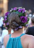 Kobieta ze spiętymi włosami i kolorowym kwiatowym wiankiem na głowie, z tyłu, górna część ciała, tło rozmyte, ulica, ludzie