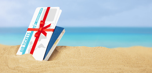 Air tickets as  gift with red ribbon and bow. Passport and air tickets in the sand on the beach of the sea