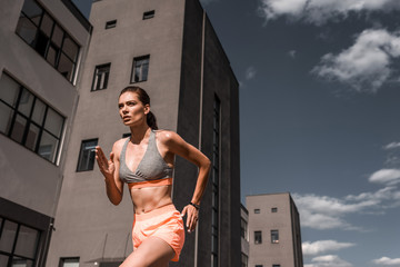 Wall Mural - young concentrated sportswoman running with fitness tracker in city