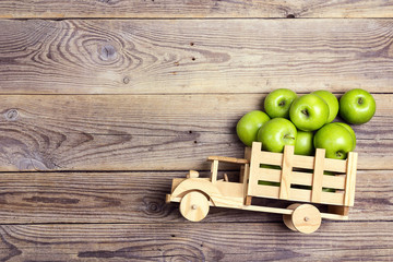 Toy wooden truck with green apples in the back on wooden  background.