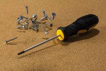 Screwdriver And Scattered Screws On Wooden Background