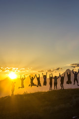 group of people with hands up jumping on grass in sunset mountains