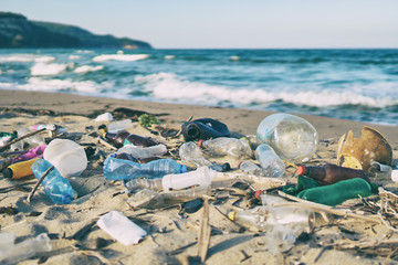 Wall Mural - Spilled garbage on the beach of the big city. Empty used dirty plastic bottles. Dirty sea sandy shore the Black Sea. Environmental pollution. Ecological problem. Bokeh moving waves in the background  