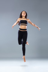 Sticker - Attractive excited fitness girl, ballerina dancer in sportwear jumping of joy isolated over gray background.