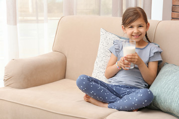 Sticker - Cute little girl with glass of milk on sofa at home