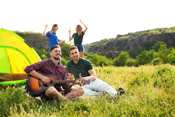 Wall Mural - Group of young people resting with beer and guitar near camping tent in wilderness