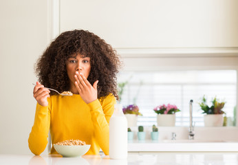 Poster - African american woman eating cereals and milk at home cover mouth with hand shocked with shame for mistake, expression of fear, scared in silence, secret concept