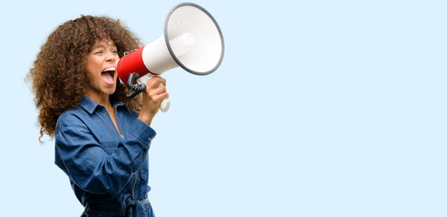 african american woman wearing blue jumpsuit communicates shouting loud holding a megaphone, express
