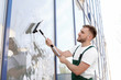 Male cleaner wiping window glass with squeegee from outside