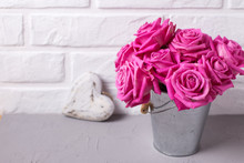 Bright Pink Roses Flowers In Bucket And  Heart On Grey Background Against White Wall.