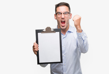 Sticker - Handsome young business man showing a clipboard annoyed and frustrated shouting with anger, crazy and yelling with raised hand, anger concept