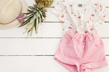 Pink denim shorts and shirt, straw hat, pineapple. White Old Wooden Background