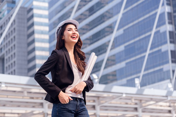 Portrait of Happy professional construction engineer woman holding the blueprint and wearing the safety helmet and glasses at the building site place background,