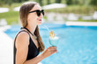 © rh2010 - Young woman in black swimsuit relaxing with summer cocktail sitting on the poolside outdoors