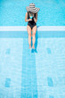 © rh2010 - Young woman in black swimsuit and sun hat relaxing with cocktail in the swimming pool outdoors