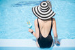 © rh2010 - Young woman in black swimsuit and sun hat sitting back with cocktail in the swimming pool outdoors